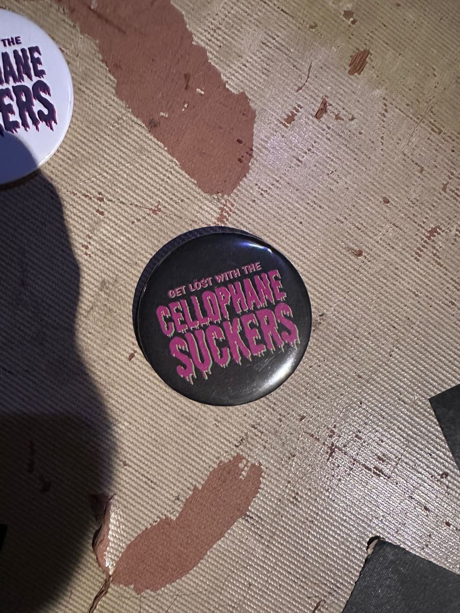 Black pin button reading Get lost with the Cellophane Suckers