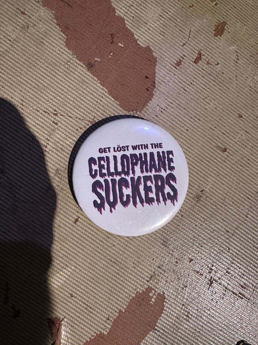 White pin button reading Get lost with the Cellophane Suckers